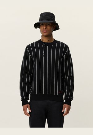 Black knit sweater with white vertical stripes, round neck, ribbed cuffs, and hem. Worn with a black bucket hat.