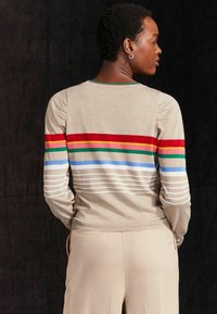 Pull beige avec des rayures horizontales multicolores en rouge, vert, jaune et bleu. Avec un col côtelé et une texture douce. Manches longues.