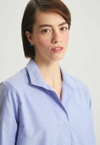 Chemise bleu de col, en tissu léger ; présente un design simple avec une texture lisse et un minimum de détails de couture.