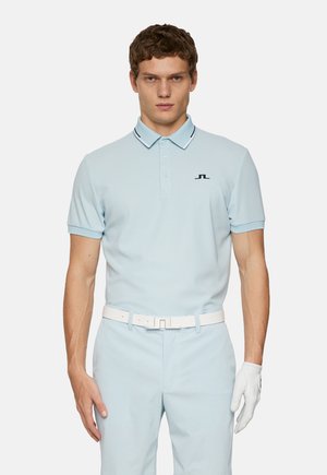 Light blue polo shirt with a tailored fit, black logo on the chest, contrasting collar trim, paired with light blue pants and white belt.