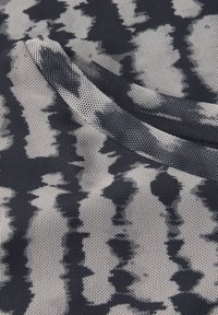 Das strukturierte Gewebe zeigt ein monochromes Muster aus dunkelgrau und weiß in abstrakten Formen, mit einem glatten Ausschnitt, der das Design hervorhebt.