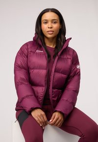 Burgundowa kurtka puchowa z kapturem, z pikowanymi sekcjami i logo na piersi. Nosi się ją na dopasowane, długie rękawy i legginsy.