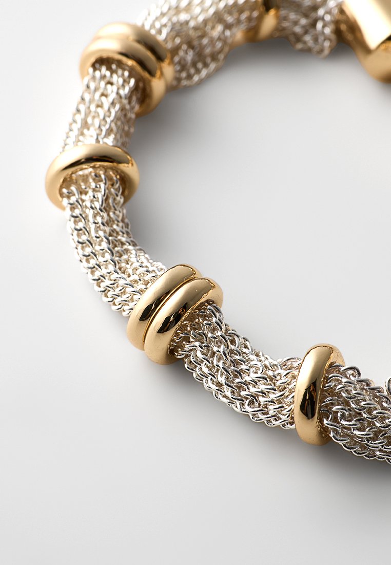 Bracelet en maille argentée avec plusieurs anneaux en or poli régulièrement espacés le long de sa longueur, présenté sur une surface blanche.