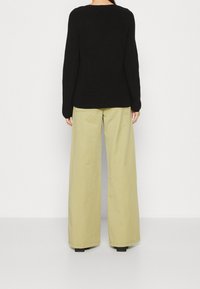 Schwarzer gestrickter Pullover mit langen �Ärmeln, kombiniert mit hellen khakifarbenen weit geschnittenen Hosen. Der Stoff wirkt dick und strukturiert.