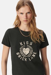 Camiseta negra de manga corta con un gráfico blanco desgastado que dice "Kiss Brick Lane" rodeado de un diseño de hojas.