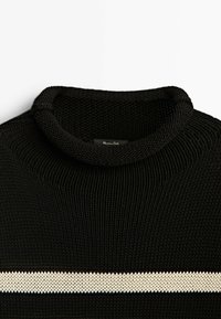 Svart stickad tröja med ribbad textur, med ett vitt horisontellt streck över bröstet och rundad krage.