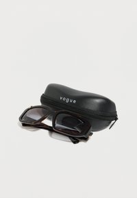 Μαύρα ορθογώνια γυαλιά ηλίου με ταρταρούγα και σκούρους φακούς, τοποθετημένα δίπλα σε μια κλειστή μαύρη θήκη με φερμουάρ με την ετικέτα «vogue».