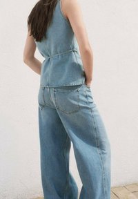 Lyseblåt denimoutfit med en tætsiddende, ærmeløs top og bukser med vide ben. Bemærkelsesværdig syningsdetalje og baglommer på bukserne.