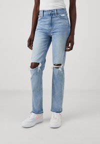 Jeans azzurri a vita alta con strappi alle ginocchia, realizzati in tessuto denim. Indossati con sneakers multicolori con suole bianche.