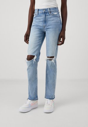Jeans azzurri a vita alta con strappi alle ginocchia, realizzati in tessuto denim. Indossati con sneakers multicolori con suole bianche.