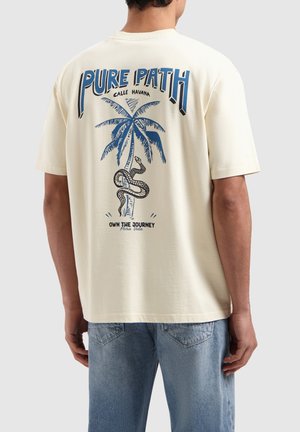 Crème-kleurig katoenen t-shirt met een blauwe grafische ontwerp van palmbomen en een slang. De tekst luidt "PURE PATH" en "OWN THE JOURNEY."