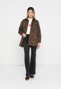 Giacca leopardata con chiusura a bottoni, maniche lunghe e colletto, abbinata a una maglietta bianca e jeans neri a palazzo. Scarpe con tacco nero.