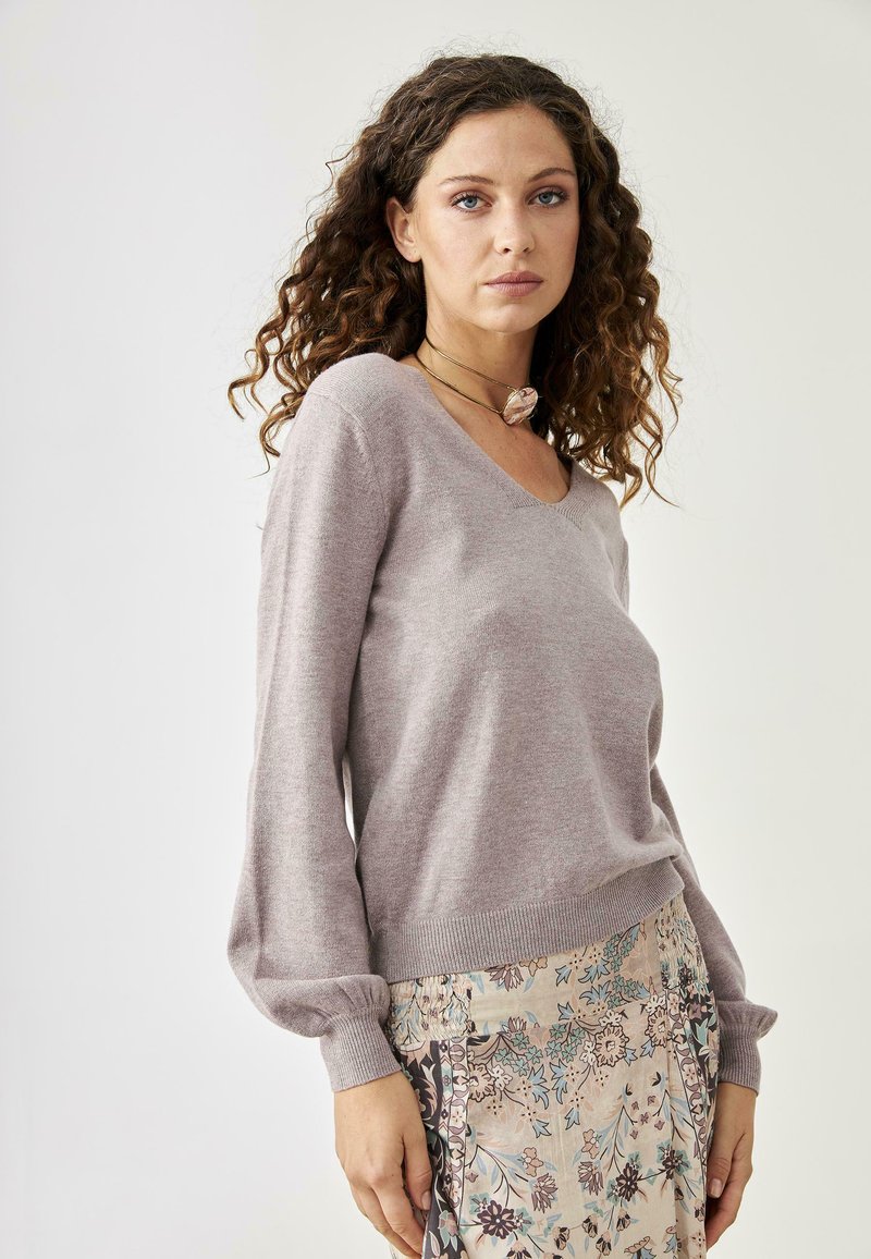 Suéter de punto de color púrpura claro con escote en V, mangas largas de globo y dobladillo acanalado, combinado con una falda de estampado floral.