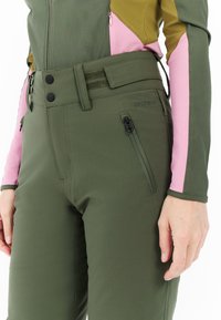 Close-up of person wearing olive green pants with zipper pocket and adjustable waist, paired with a green and pink long-sleeve top.