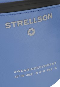 Produkt aus blauem strukturiertem Leder mit geprägt eingraviertem Markennamen "STRELLSON" und Koordinaten, verziert mit silbernem Kreuzakzent und Hashtag-Detail.