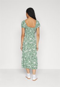 Zielona kwiatowa sukienka midi z krótkimi bufkowymi rękawami, marszczonym górnym partem i wielowarstwową spódnicą. Noszona z białymi trampkami, z odkrytą kostką.