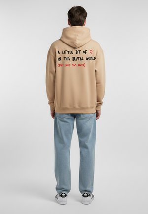 Beige hoodie met zwarte en rode tekst op de achterkant. De tekst zegt "Een beetje liefde in deze brute wereld (maar niet te veel)." Casual fit.