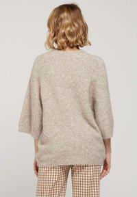 Pull oversized beige clair avec des manches trois-quarts et un tissu doux et texturé. Porté avec un pantalon à carreaux marron, au design minimaliste.