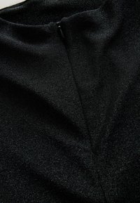 Suurel lähivõtmes must kangas, millel on nähtav lukk ja peen läikiv tekstuur, tuues esile rõiva kaelaaugu ja õmbluste detailid.