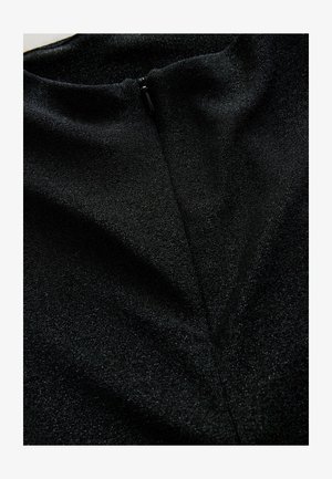 Zbliżenie na czarną tkaninę z widocznym zamkiem błyskawicznym i subtelnym błyszczącym wykończeniem, podkreślające dekolt i szczegóły szwów odzieży.