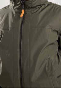 Olivově zelená bunda z hladké, lehké látky s celým zipem, kapucí a oranžovým detailem na jezdcích zipu. Má přední švy.