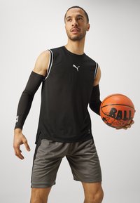 Camiseta atlética negra con detalles blancos, pantalones cortos grises y mangas negras; sosteniendo un balón de baloncesto naranja con "BALL" impreso en él.