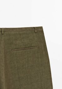 Vue arrière d'un pantalon en lin vert olive montrant des passants de ceinture et une poche à encoche unique sur fond blanc.
