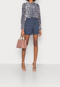 Navy blue shorts in a tailored design, paired with a white and navy spotted blouse. Accessorized with a pink handbag and nude strappy heels.