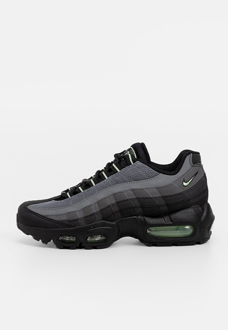 Baskets Nike Air Max 95 noires et grises avec des amortisseurs d'air verts visibles et des accents verts sur les boucles de lacets et le logo sur un fond blanc.
