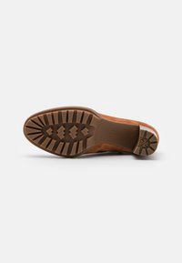 Scarpa scamosciata marrone chiaro con suola in gomma texturizzata caratterizzata da profonde scanalature per una migliore trazione e un tallone di supporto. Design pulito senza decorazioni.