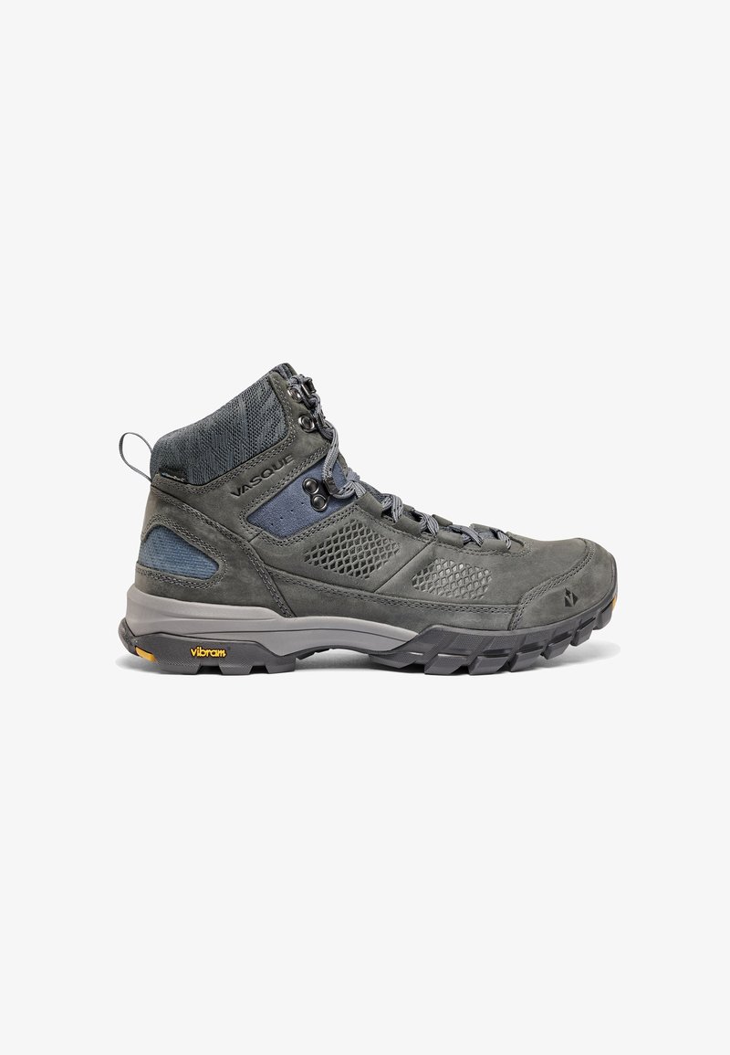 Bota de senderismo gris que combina materiales de cuero y malla, con soporte alto para el tobillo, acentos texturizados y suela Vibram para mayor tracción.