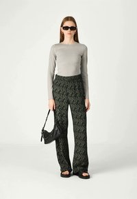 Grå langermet topp, mønstrede grønne vide bukser, svart veske og flate svarte sandaler. Solbriller fullfører antrekket.