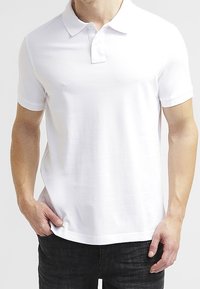 Polo blanc à manches courtes avec col, patte de boutonnage à trois boutons et légère texture, associé à un jean foncé.