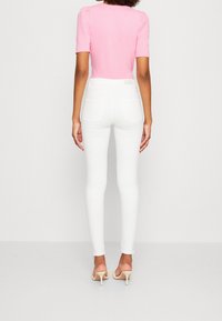 Jeans blancos ajustados con una cintura alta, bolsillos traseros sutiles, combinados con una blusa de color rosa claro con mangas cortas abullonadas. Textura suave en todo.