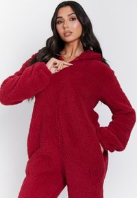 Mono de forro polar rojo con capucha, que presenta un tejido suave y texturizado, mangas largas y un cierre frontal con cremallera. Apto para uso casual.
