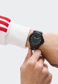 Must mustriga musta analoogkell tekstureeritud kummirihmaga ja ümmarguse näoga. Valged tunniindikaatorid ja käed kontrastivad musta diali taustaga.