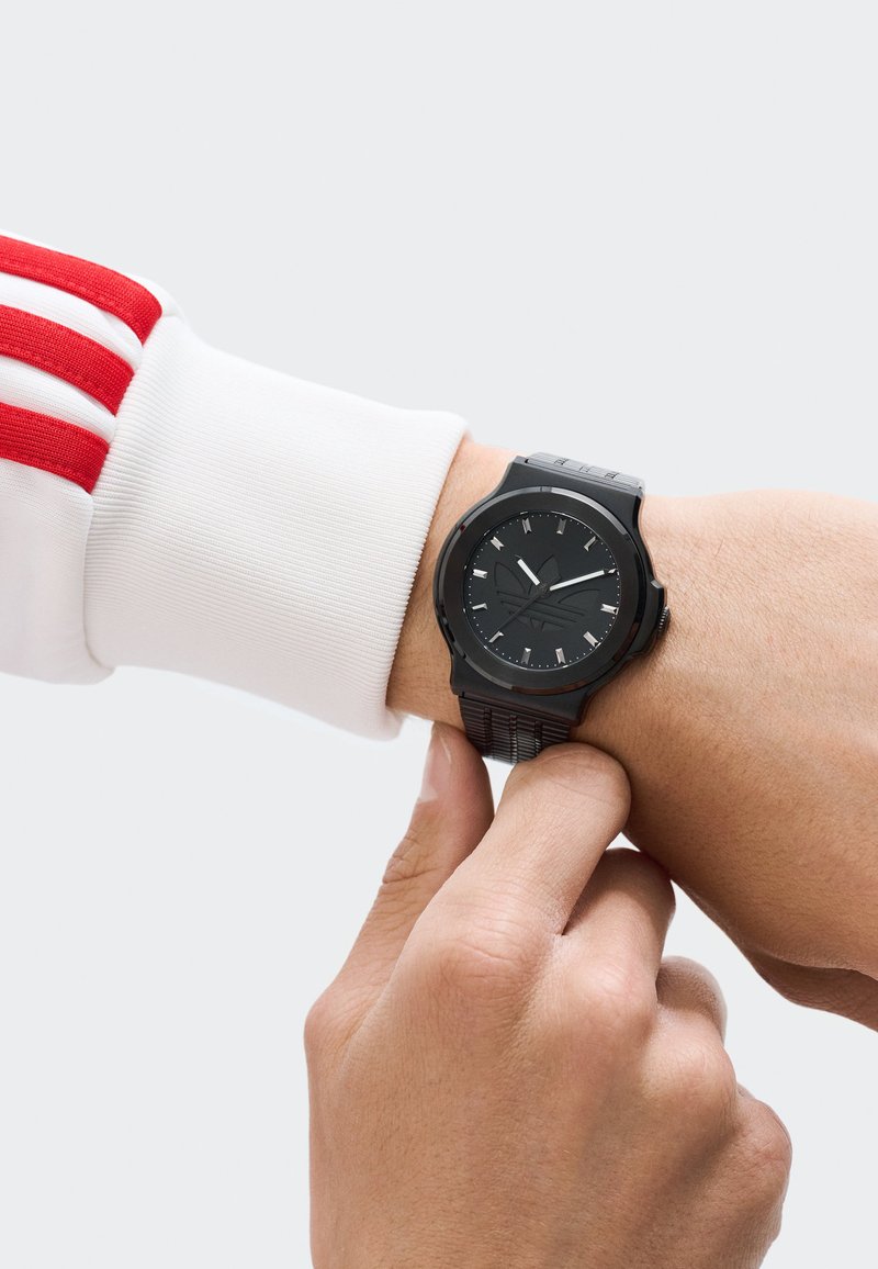 Must mustriga musta analoogkell tekstureeritud kummirihmaga ja ümmarguse näoga. Valged tunniindikaatorid ja käed kontrastivad musta diali taustaga.