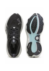 Chaussures de sport noires avec un dessus en mesh texturé, semelle blanche rembourrée et semelle extérieure en caoutchouc avec un motif en vagues. Des accents incluent un logo.