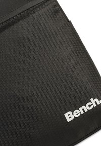Zwarte textielen zak met een hexagonaal patroon, voorzien van een ritssluiting en een wit "Bench." logo in de rechterbenedenhoek.