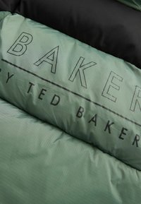 Grüner Puffermantelstoff mit einem subtilen Karomuster. Enthält das Wort "BAKER" in fetten schwarzen Buchstaben und einem schwarzen oberen Abschnitt.