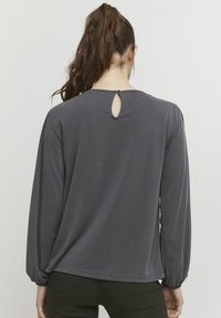 Grå langærmet bluse med rund halsudskæring og en lille nøglehulldetalje bagpå. Blødt stof med en glat overflade og afslappet pasform.