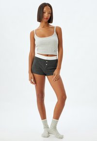 Grijze geribbelde tanktop met dunne bandjes, gecombineerd met donkergrijze gebreide shorts met een witte tailleband en knoopdetail. Lichtgrijze gestructureerde sokken.