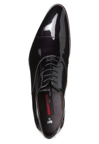 Chaussure habillée en cuir verni noir avec un bout pointu, surface lisse et laçage fermé. Étiquette intérieure visible avec le nom de la marque et le modèle.