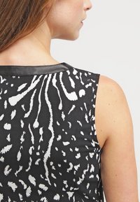 Ärmlös topp med svart bas som har ett vitt abstrakt djurmönster, accentuerad med en svart läderkant längs halsringningen.