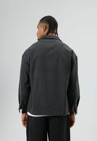 Donkergrijze wollen jas met een steekkraag, knoopmanchetten en een ontspannen pasvorm. Achteraanzicht toont een zachte textuur en een eenvoudig ontwerp.