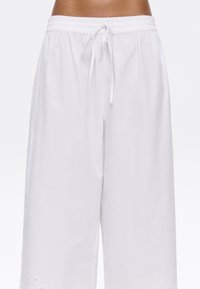 Witte katoenen wide-leg broek met een elastische tailleband en koord. Kenmerkt geborduurde details aan de zoom en een gestructureerde afwerking.