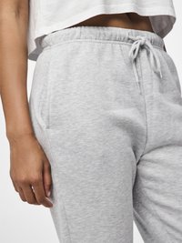 Pantaloni da tuta grigi chiari con una vita elasticizzata e cordino, dotati di tasche laterali e un tessuto morbido e strutturato.
