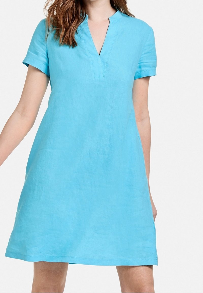 Lys blå linnedragt med korte ærmer, V-udskæring, løs pasform og minimalistisk finish. Glat tekstur, knælængde silhuet.