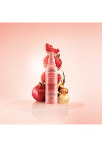Après-shampooing sans rinçage Aveda Nutriplenish dans un flacon vaporisateur rose, présenté avec des accents de grenade et de fruits sur une surface brillante.