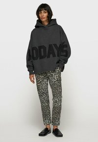 Hoodie surdimensionné gris avec "200 JOURS" en lettres noires en gras, associé à un pantalon slim en imprimé léopard et des chaussures noires à enfiler.